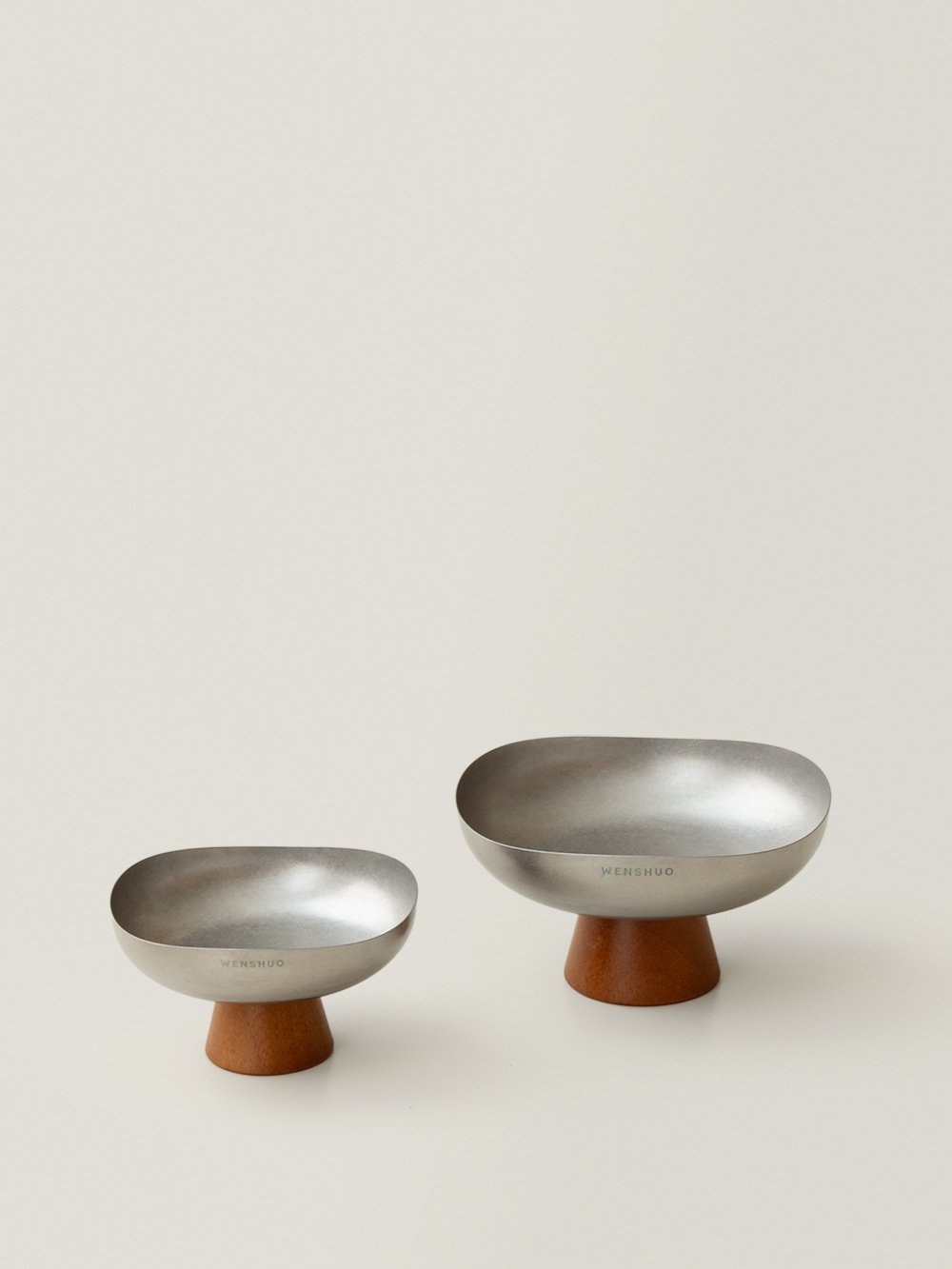 Forma stainless steel pedestal fruit bowls in two sizes on a warm grey background