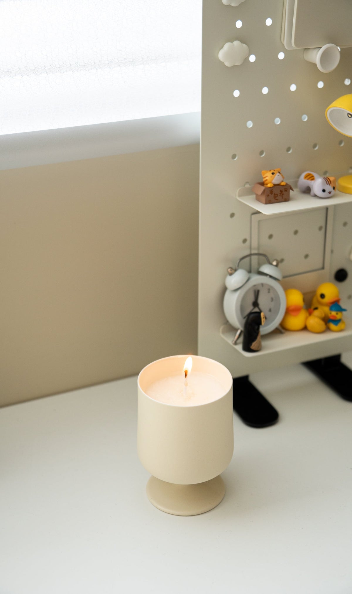 Home-made candle burning in a cream stemmed ceramic cup on a white desk