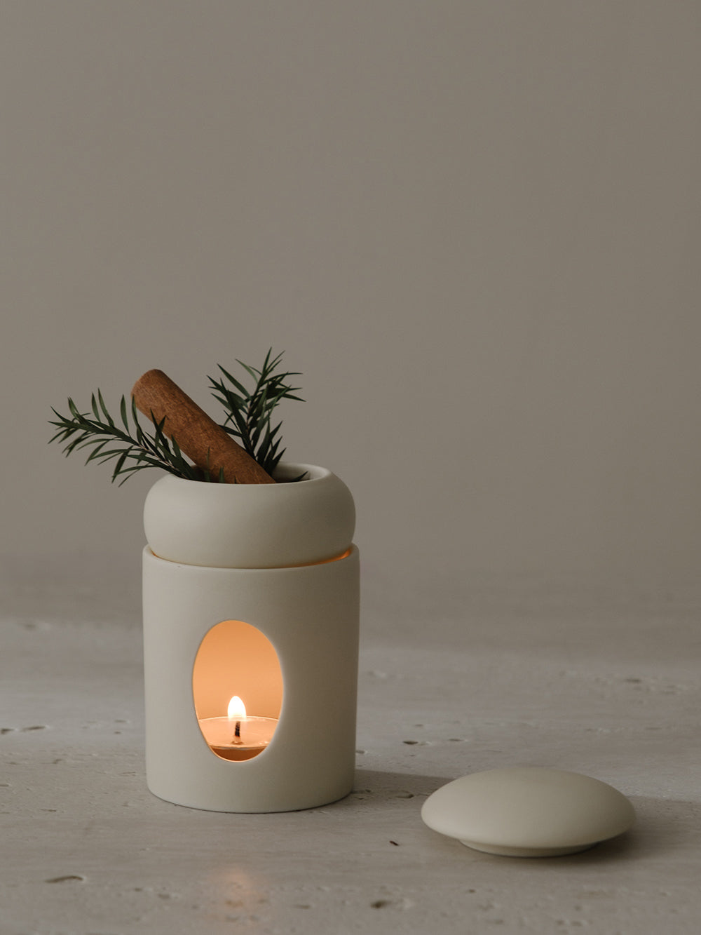Aura ceramic oil diffuser glowing from a tealight inside, with a sprig of rosemary on top