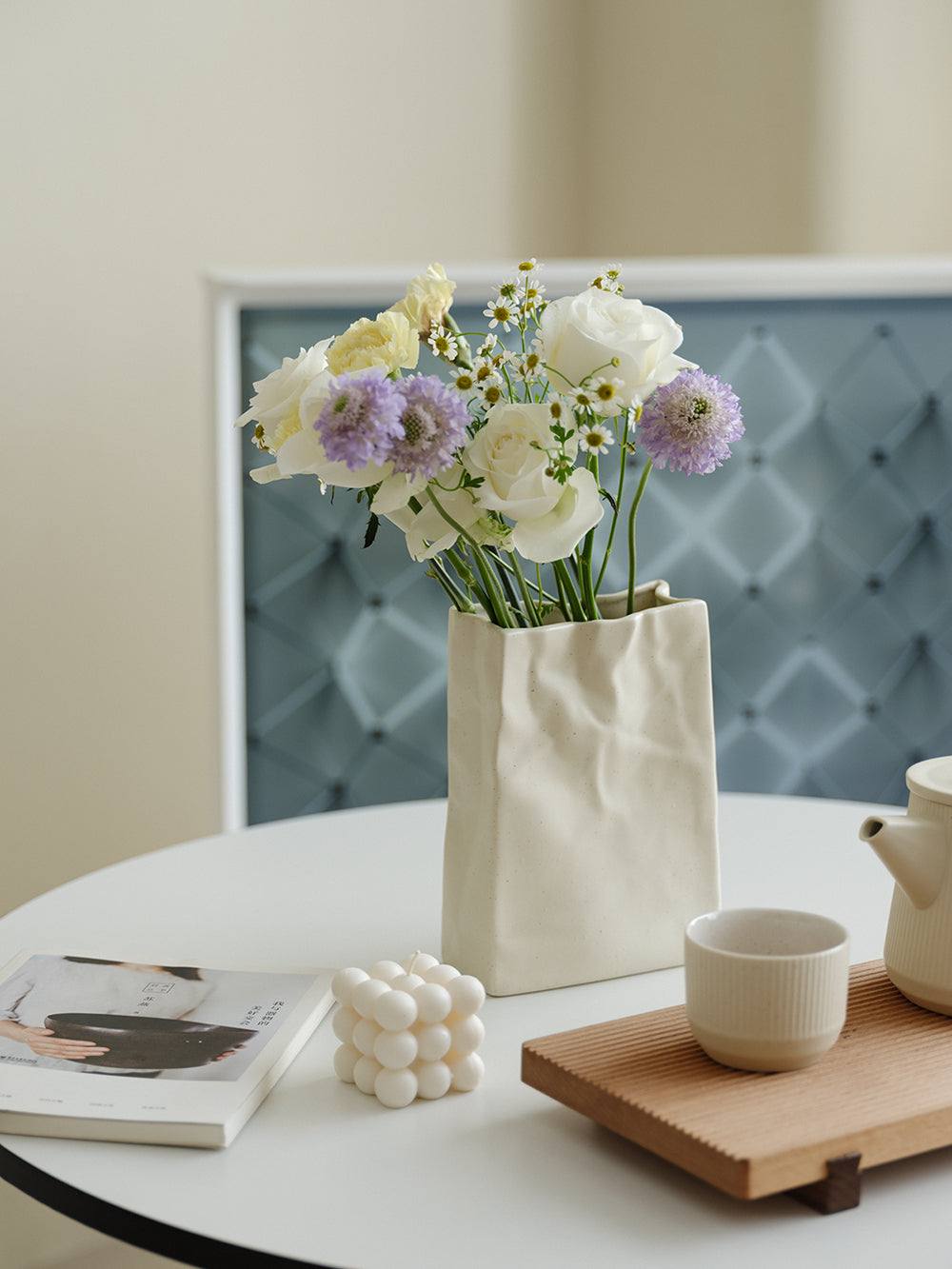 Cream ceramic paper-bag vase holding a loose bunch of fresh flowers on a round table
