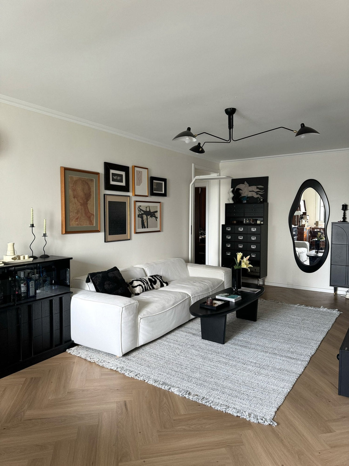 Living room in black and white with a white sofa, black oval coffee table, grey rug, gallery wall and a tall black cabinet