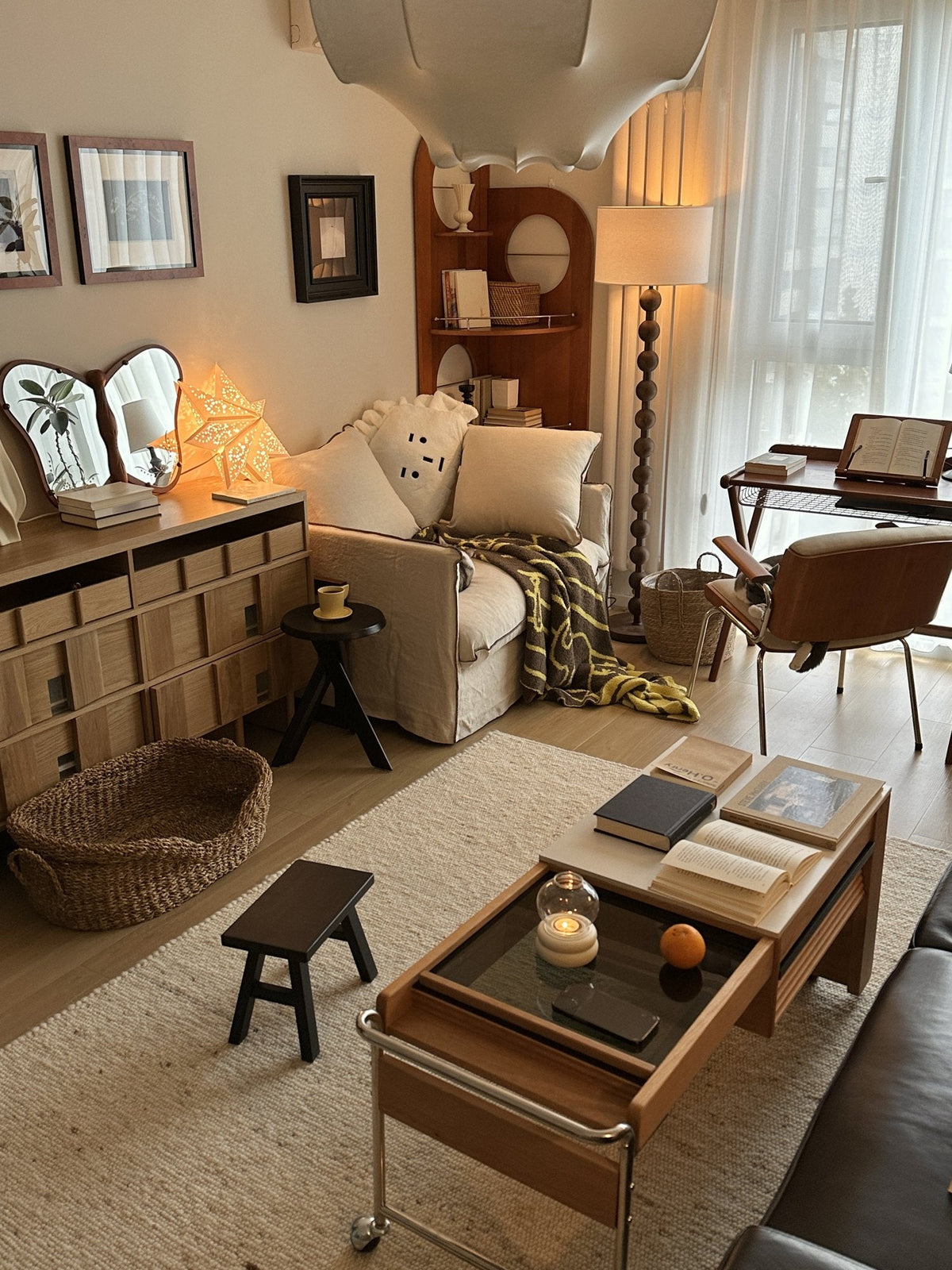 Living room with a cream sofa, wooden drawer unit, rattan basket and a wooden coffee table on castors over a jute rug, with a paper star lamp lit on the sideboard